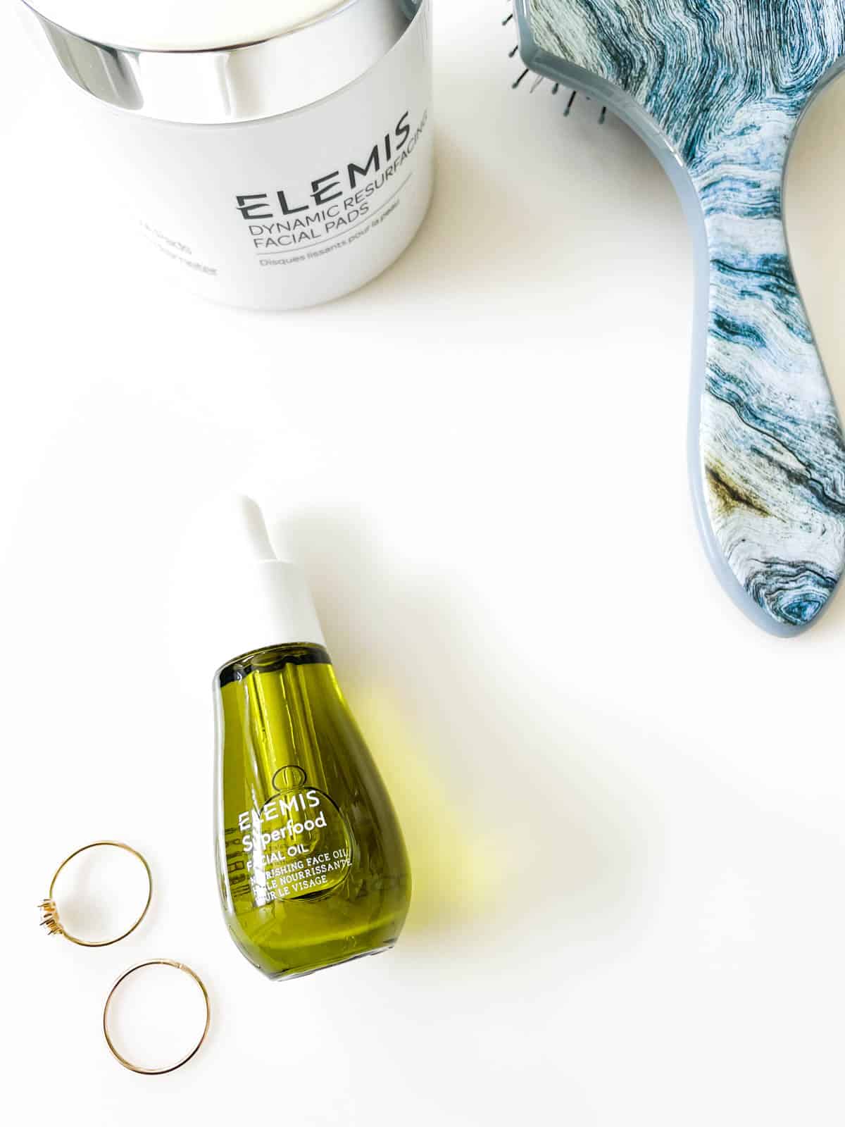 Elemis Superfood Facial Oil laying on a counter next to rings and a hairbrush.