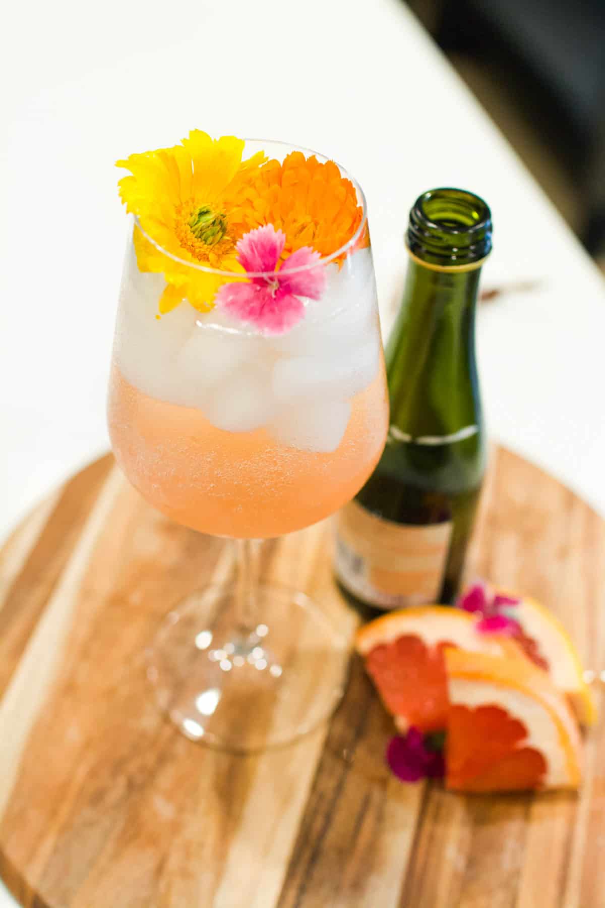 A cocktail in a wine glass on a try with flowers on top.