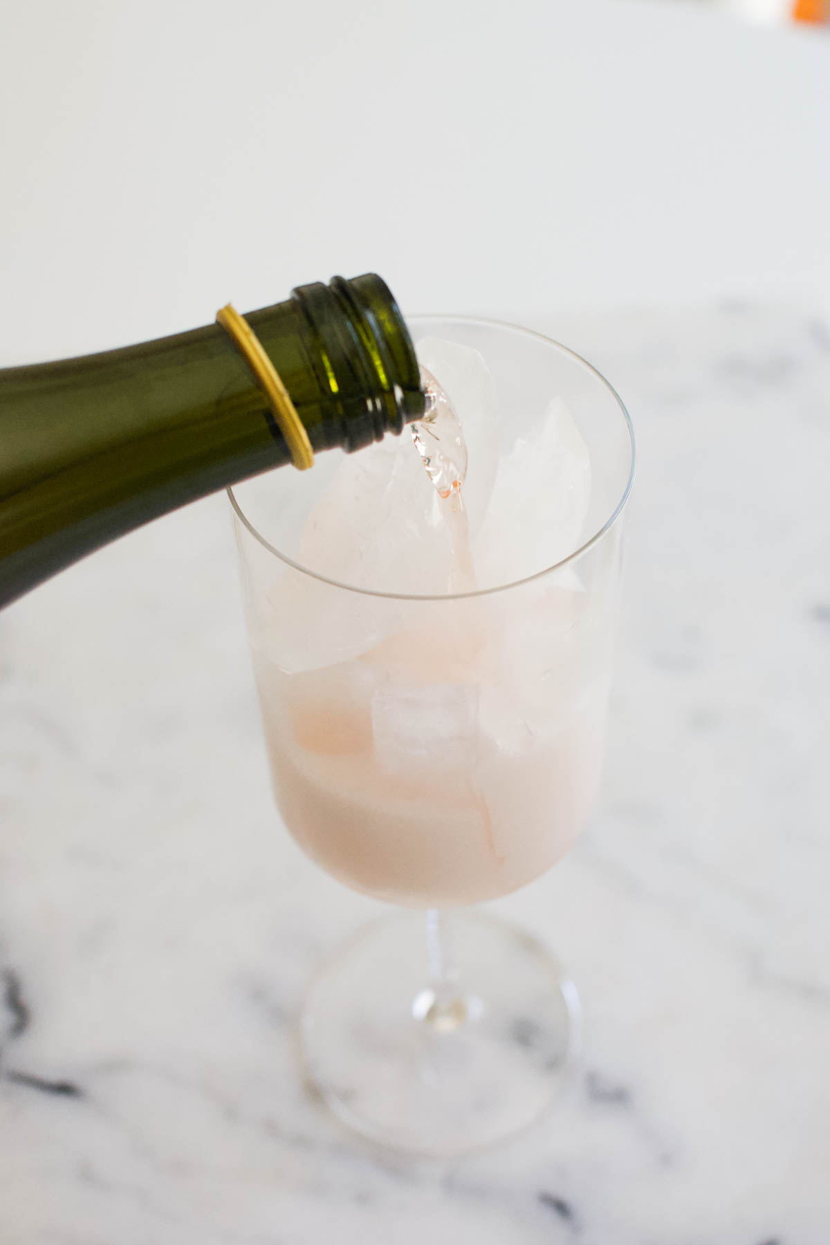 Pouring champagne over ice in a stemmed wine glass.