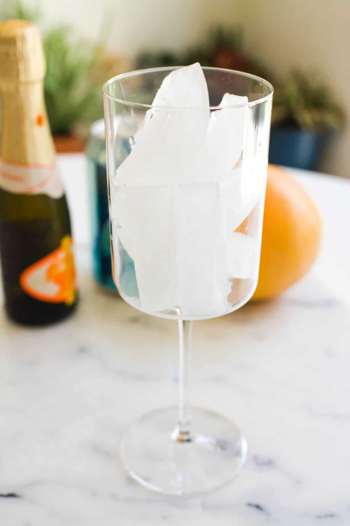 A stemmed wine glass with ice on a table.