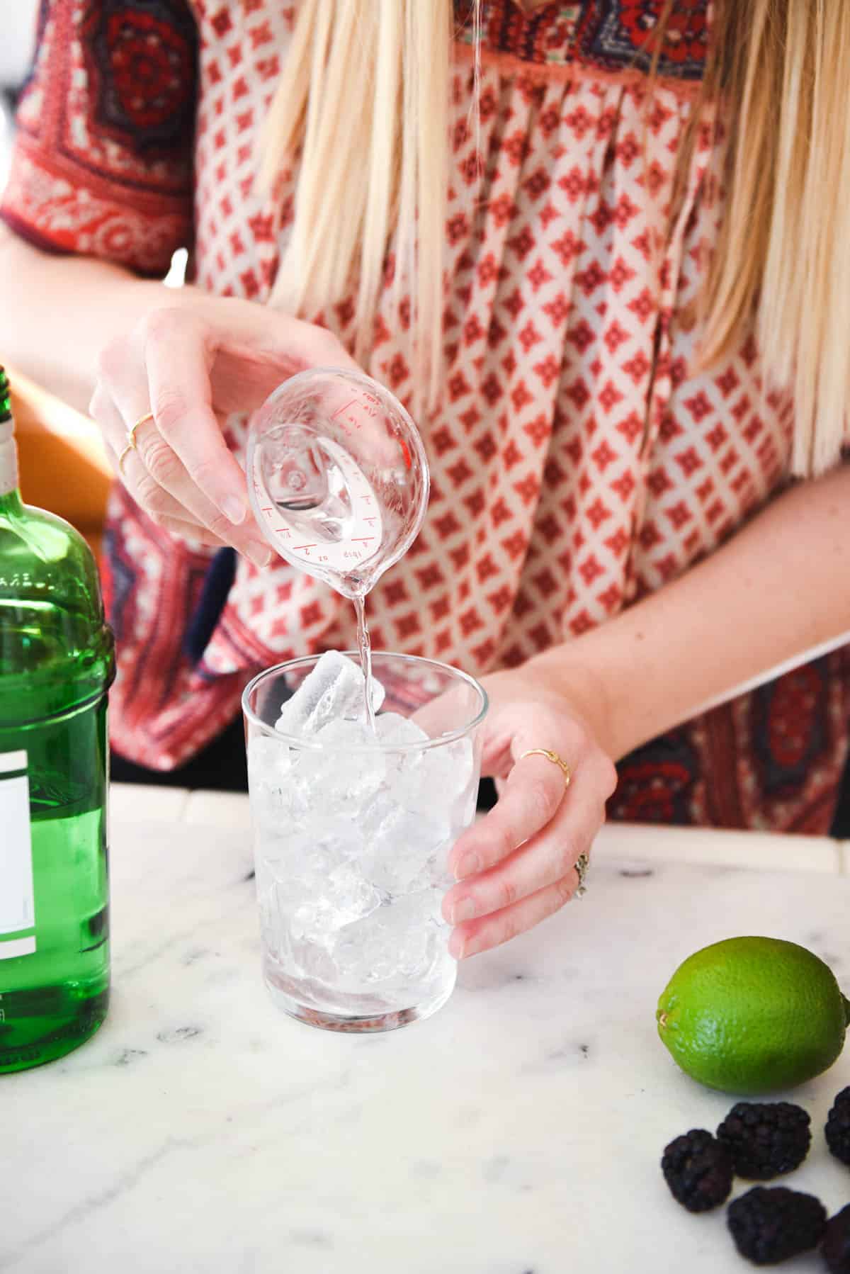 Woman adding gin to a cocktail glass filled with ice.