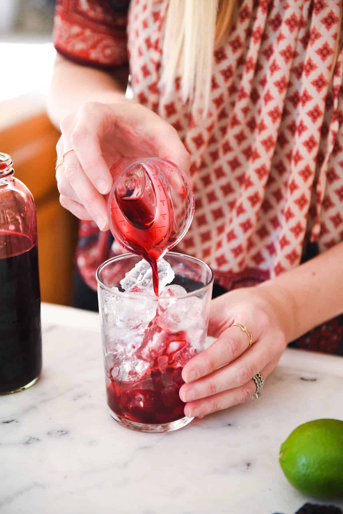 Woman adding blackberry simple syrup to a cocktail glass.