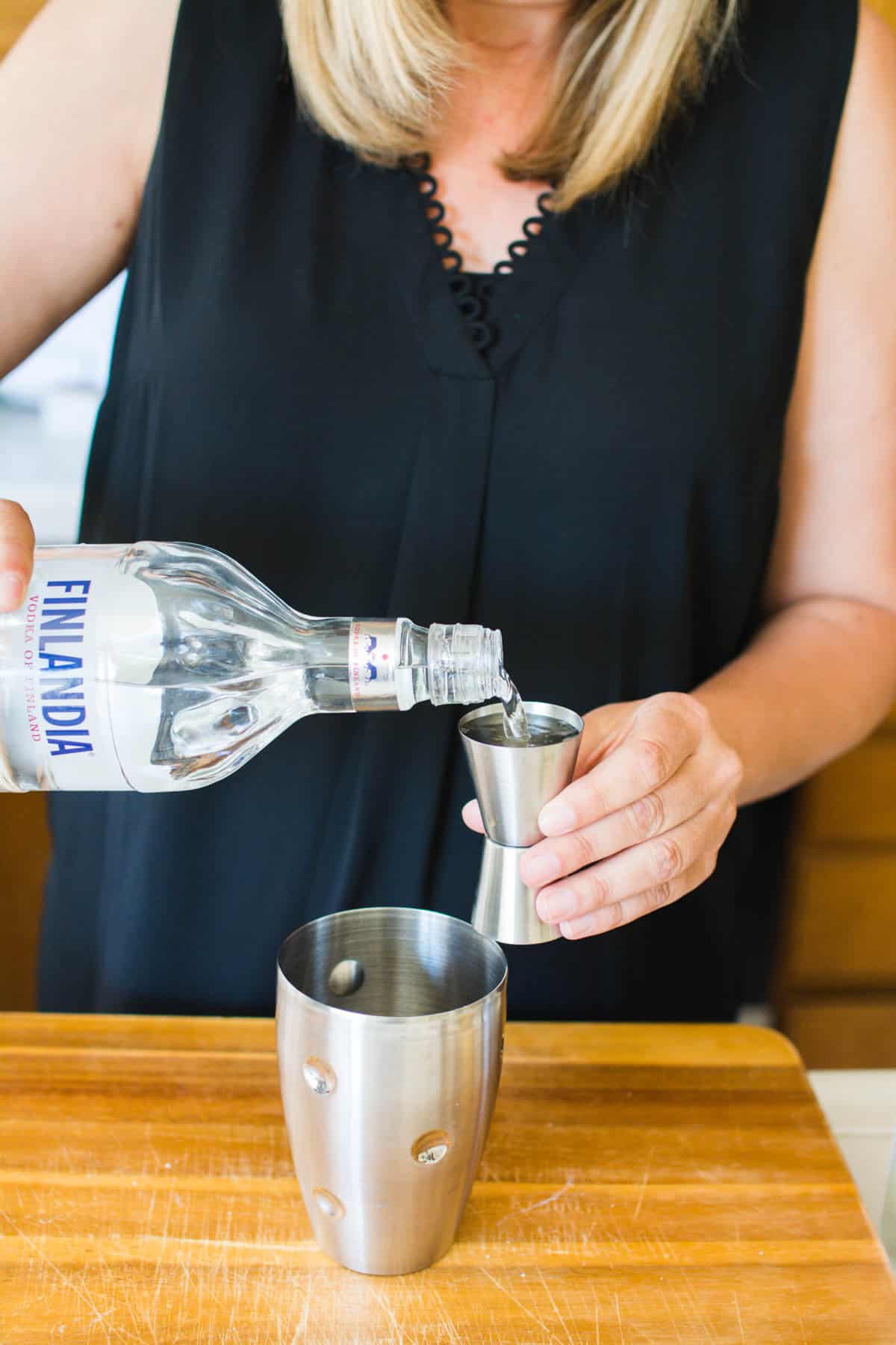 Woman adding vodka to a jigger next to a cocktail shaker. 