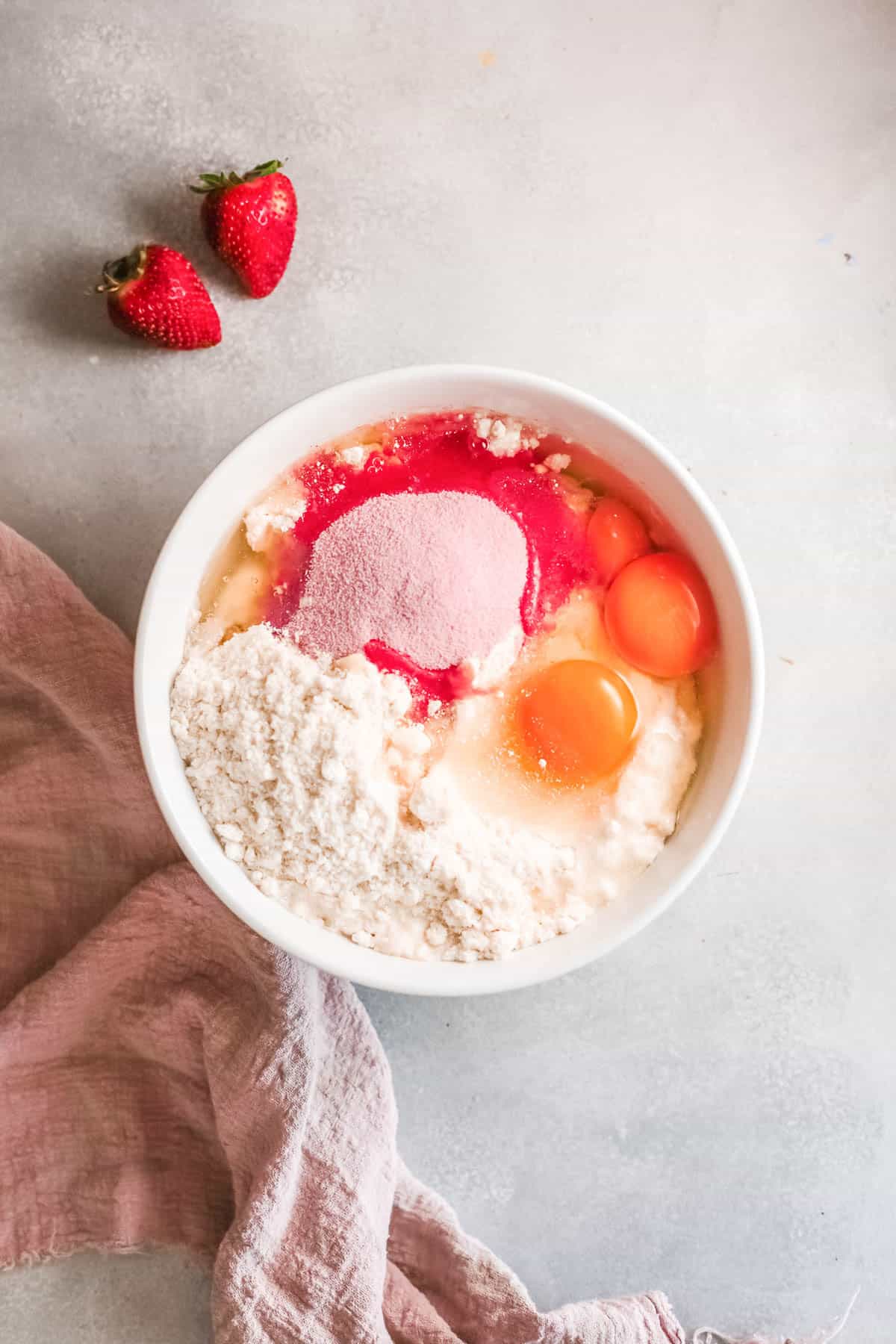 Bowl with dry cake mix, strawberry Jello powder and eggs on a counter.