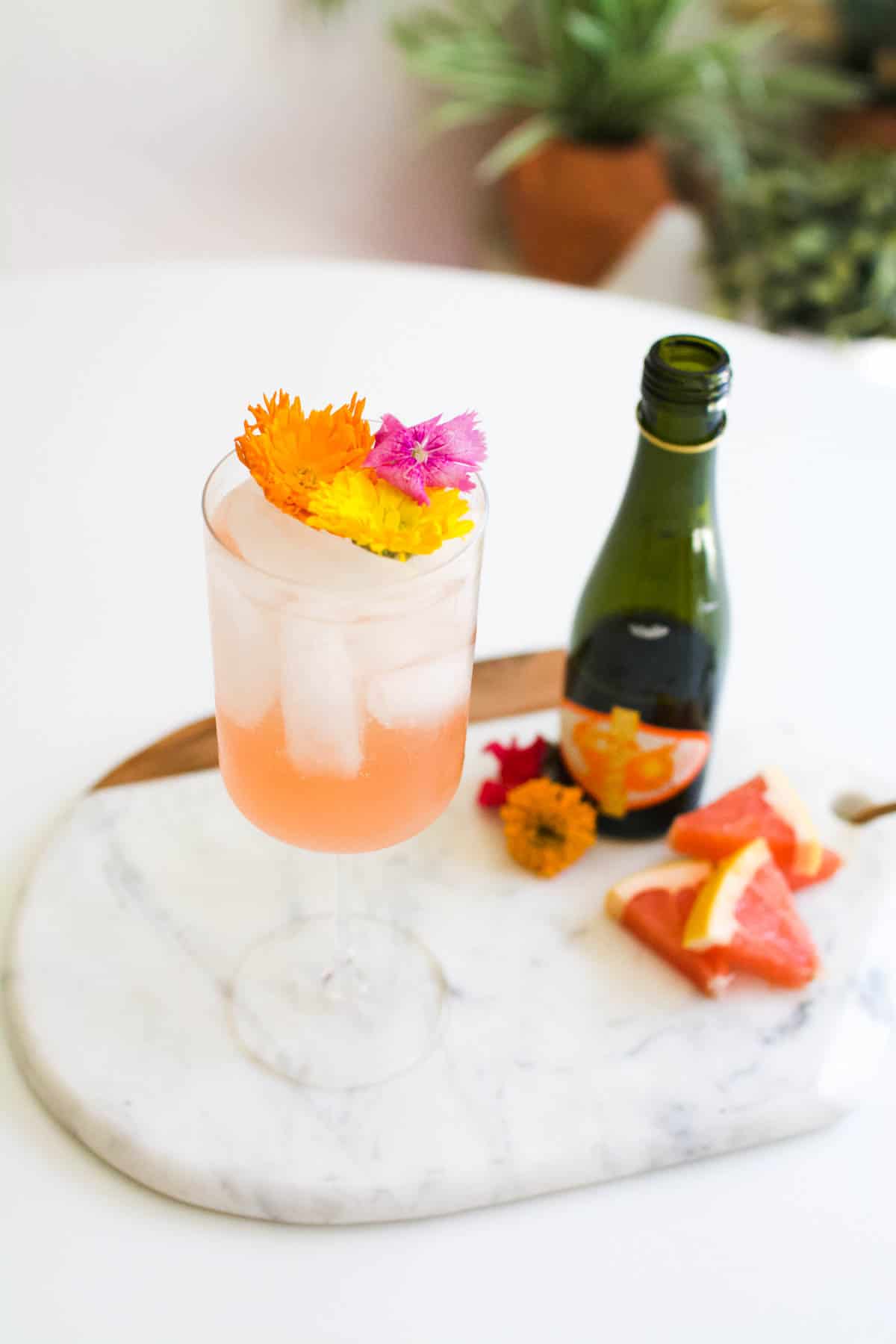 A stemmed white wine glass with a grapefruit spritzer on a serving tray with a mini bottle of champagne.