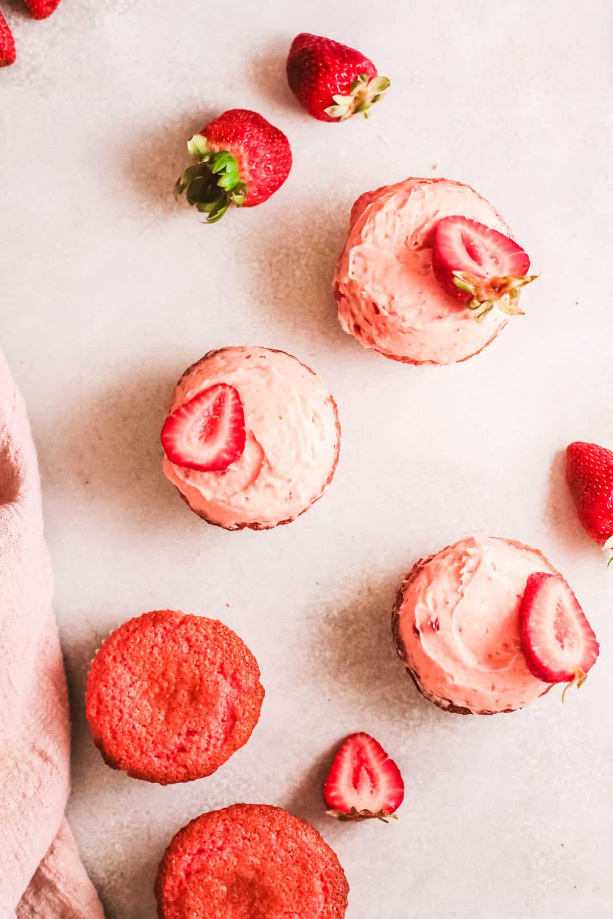 Delicious strawberry cupcakes with frosting and unfrosted on counter.