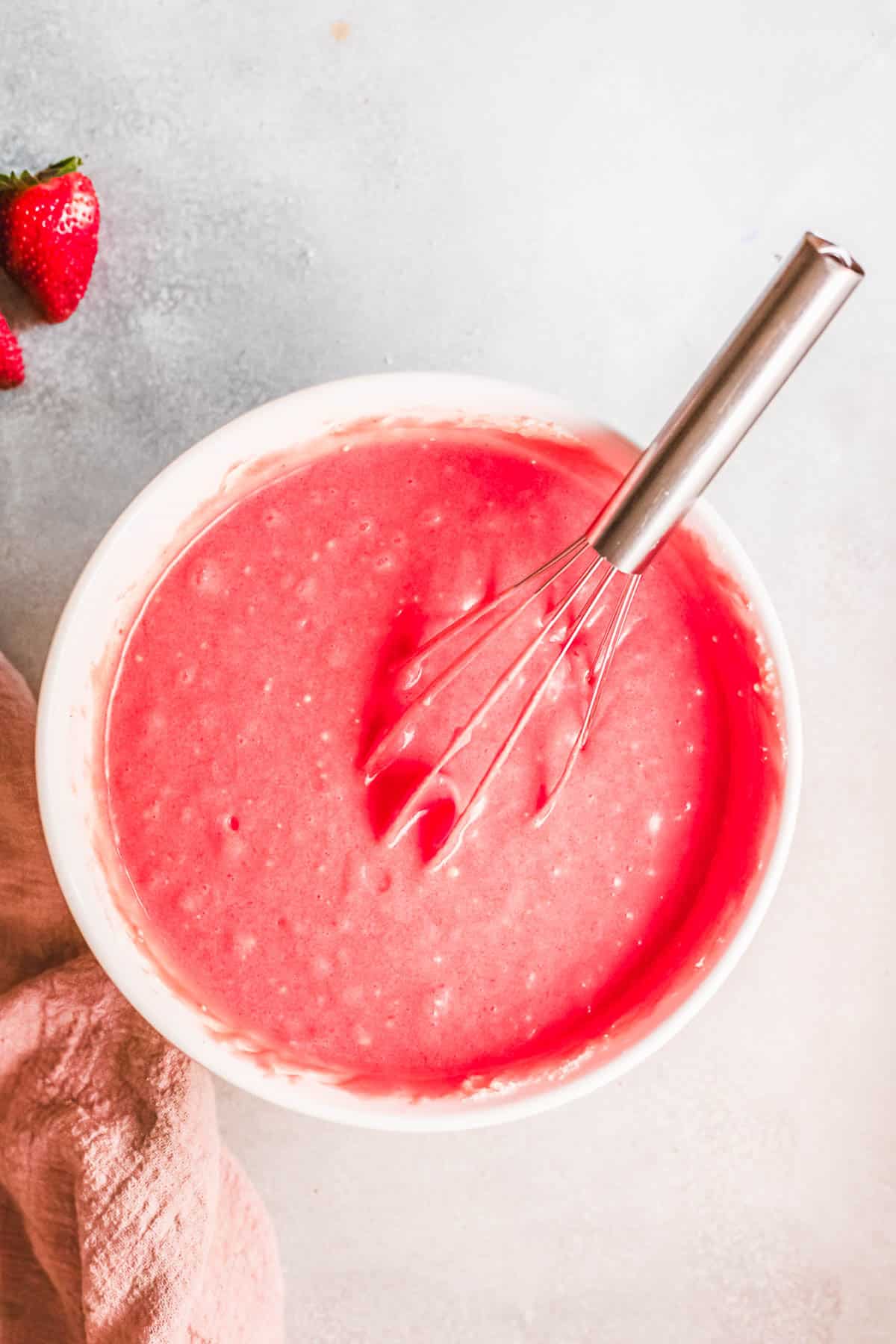 Bowl of pink cupcakes batter on a table with a whisk sticking out.