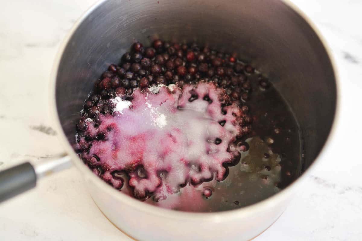 Adding the sugar to the blueberries in the saucepan to make blueberry syrup.