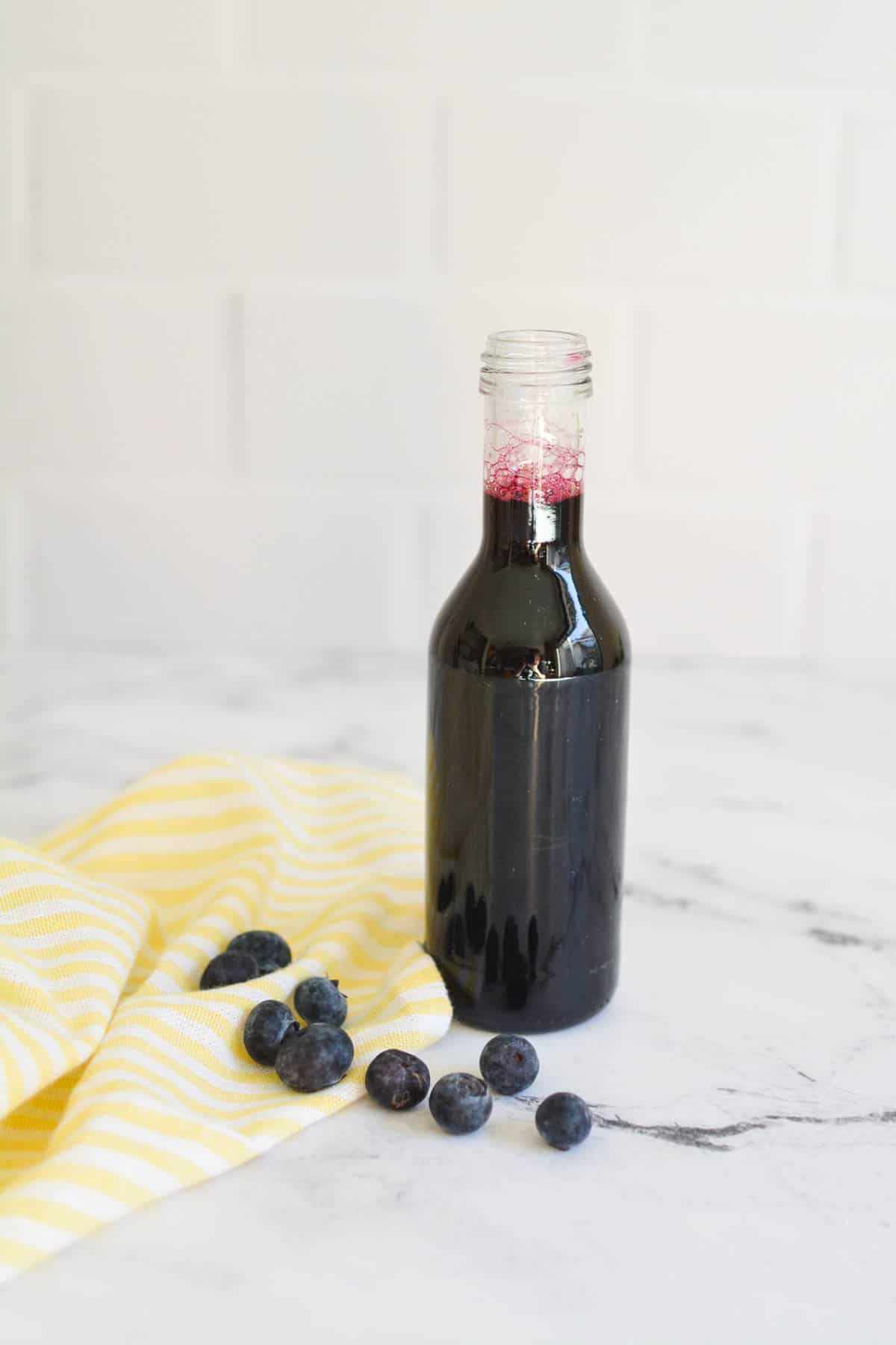 A jar of blueberry syrup with fresh blueberries laying nearby. 