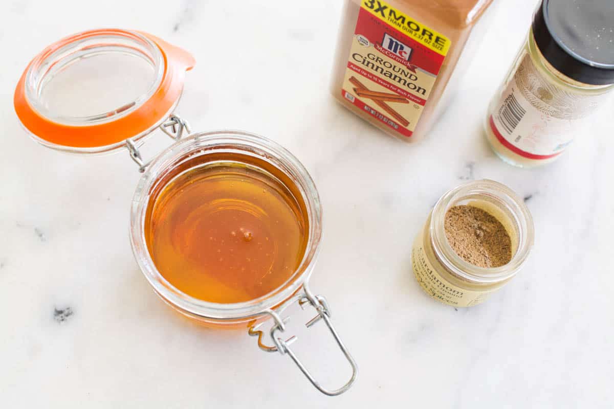 A glass jar full of honey next to spices on a counter.