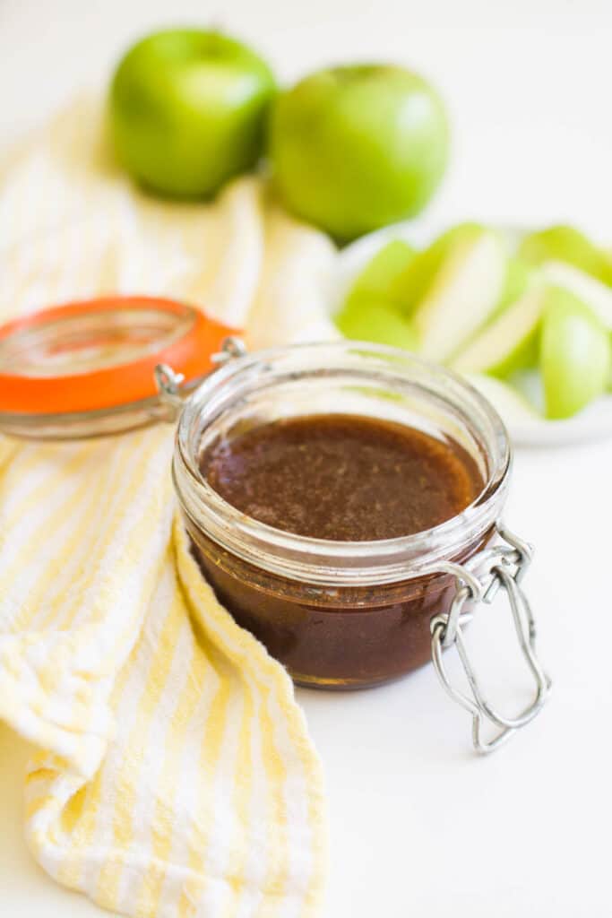 A glass jar holding a honey dip to eat with green apples.
