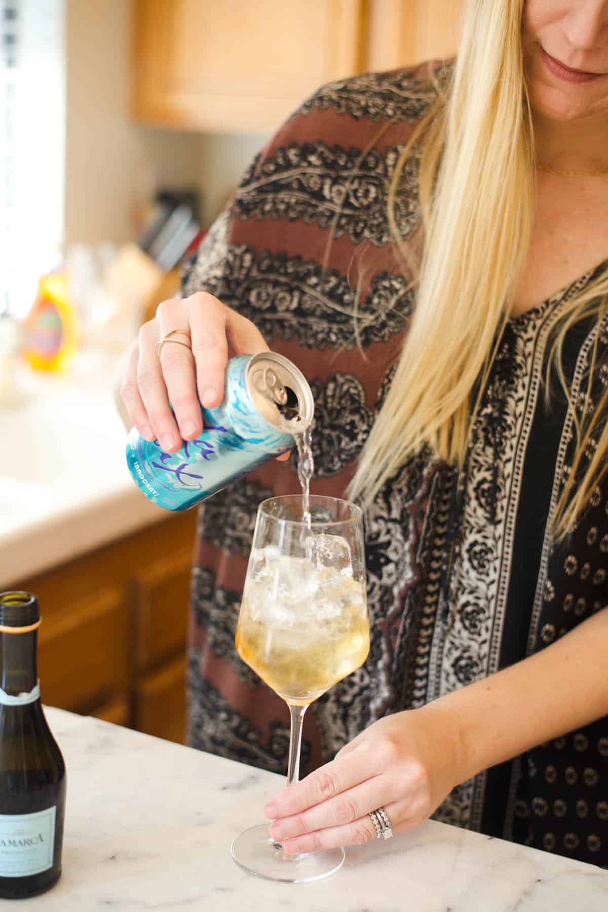 Woman pouring the soda water into a wine glass over ice.