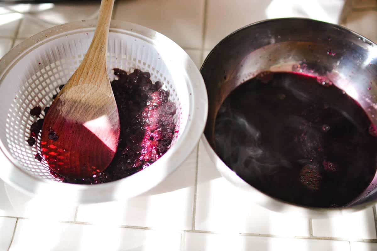 Mashing blueberries through a strainer to keep the juice.