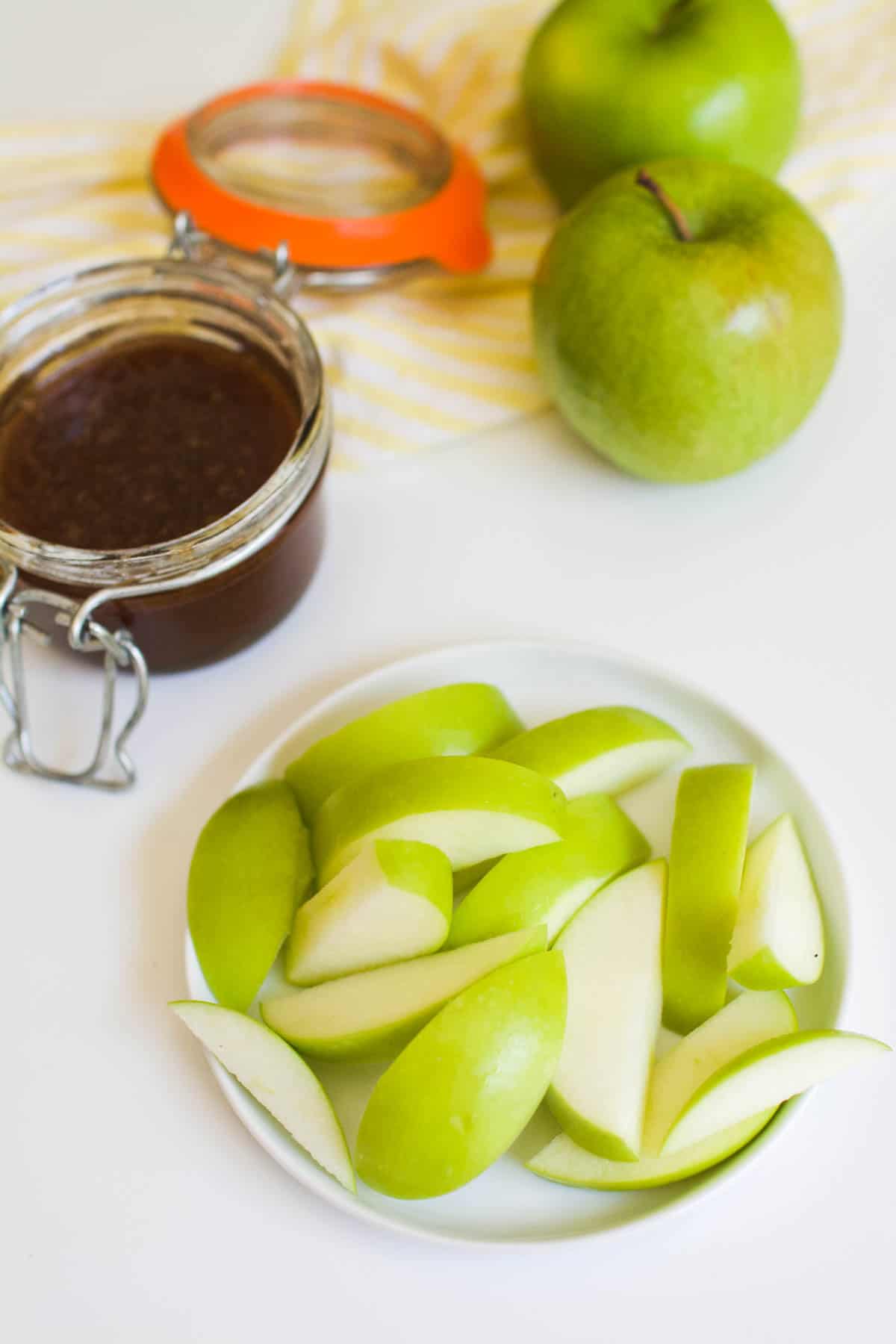 Sliced green apples on a small plate next to apple honey dip in a jar.