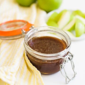 Glass jar of honey cinnamon dip with sliced apples in the background.