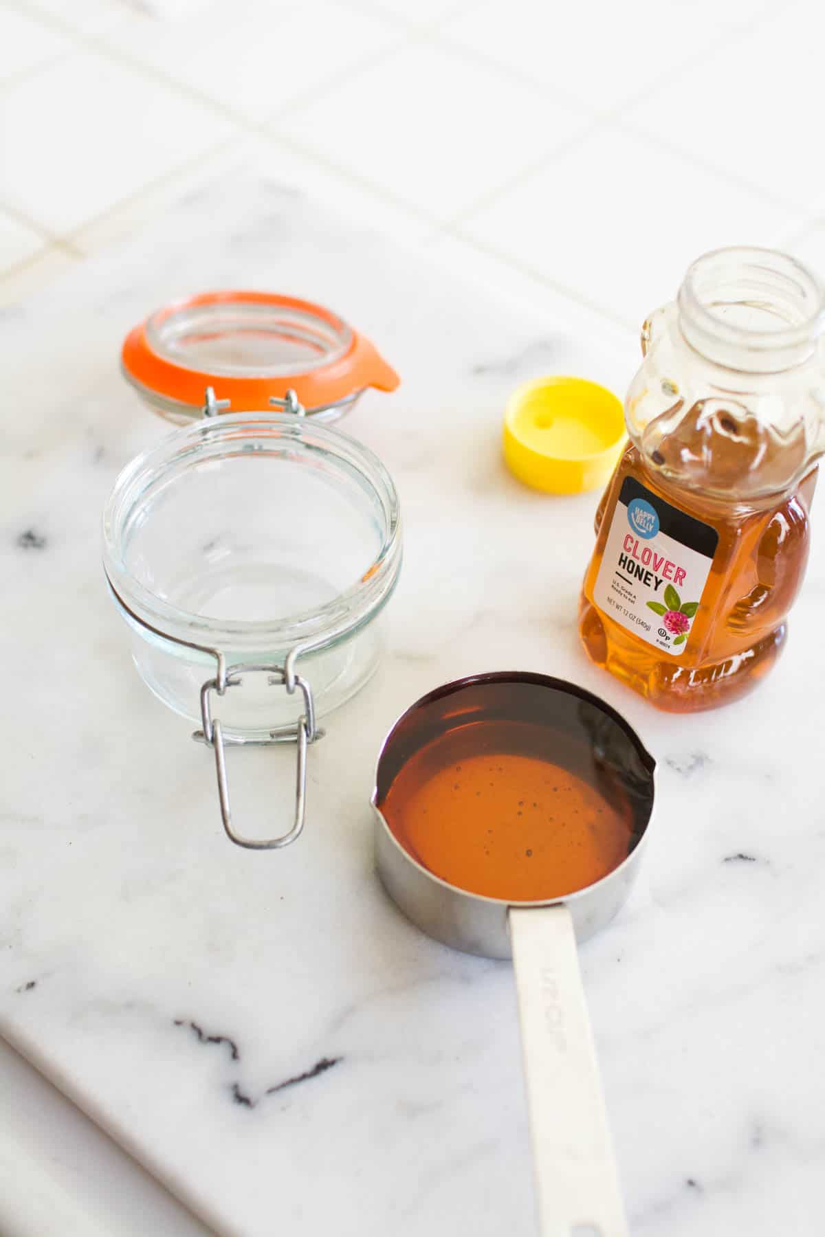 A glass jar on a counter next to a measuring cup of honey.