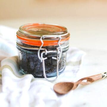 Close up image of DIY coffee scrub in a glass jar, next to a wooden scoop.