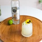 A cocktail glass holding a vodka margarita on a counter next to a bottle of vodka.