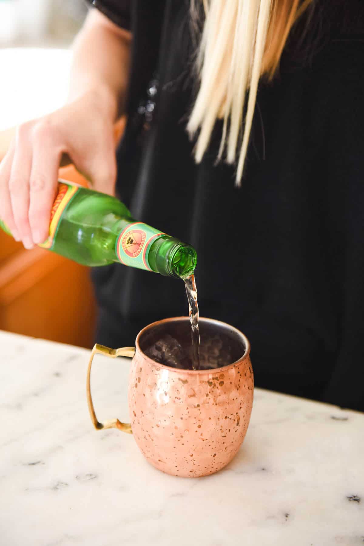 Woman adding ginger beer to a copper mug on a counter. 