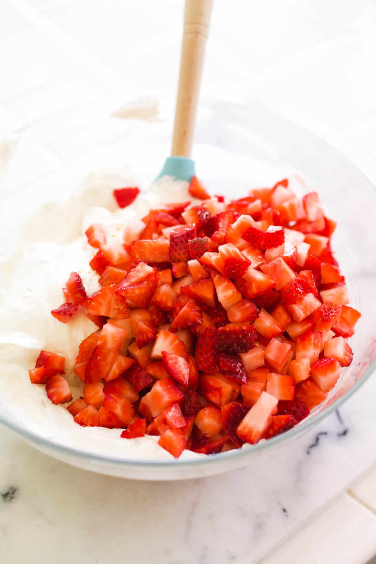 Chopped strawberries for Frozen Strawberry Yogurt Pie in a bowl with yogurt and Cool Whip.