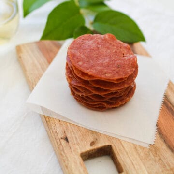 Baked Salami Chips on a white napkin sitting on a wooden cutting board.