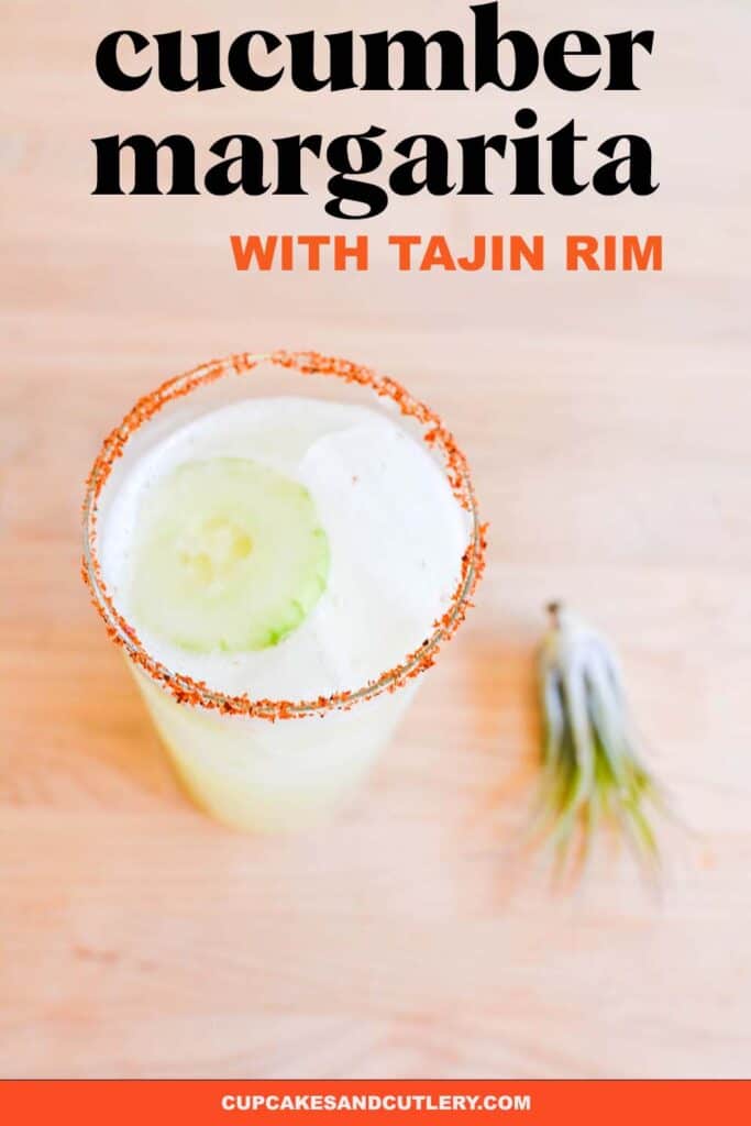 A margarita with cucumber and a Tajin rim on a table.