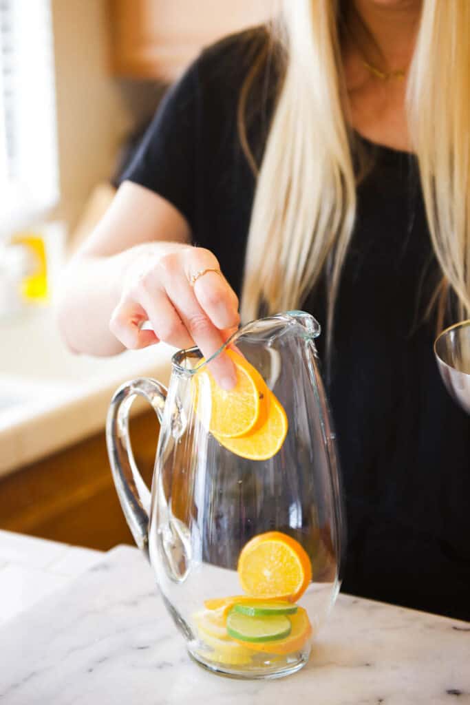 Woman putting sliced oranges into a glass pitcher.