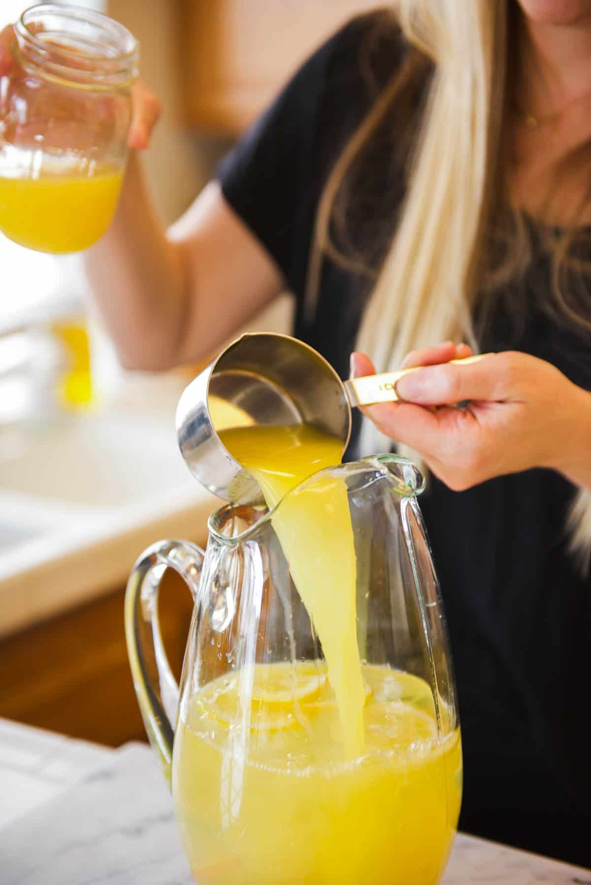 Woman adding fresh orange juice to a glass pitcher for a cocktail recipe. 