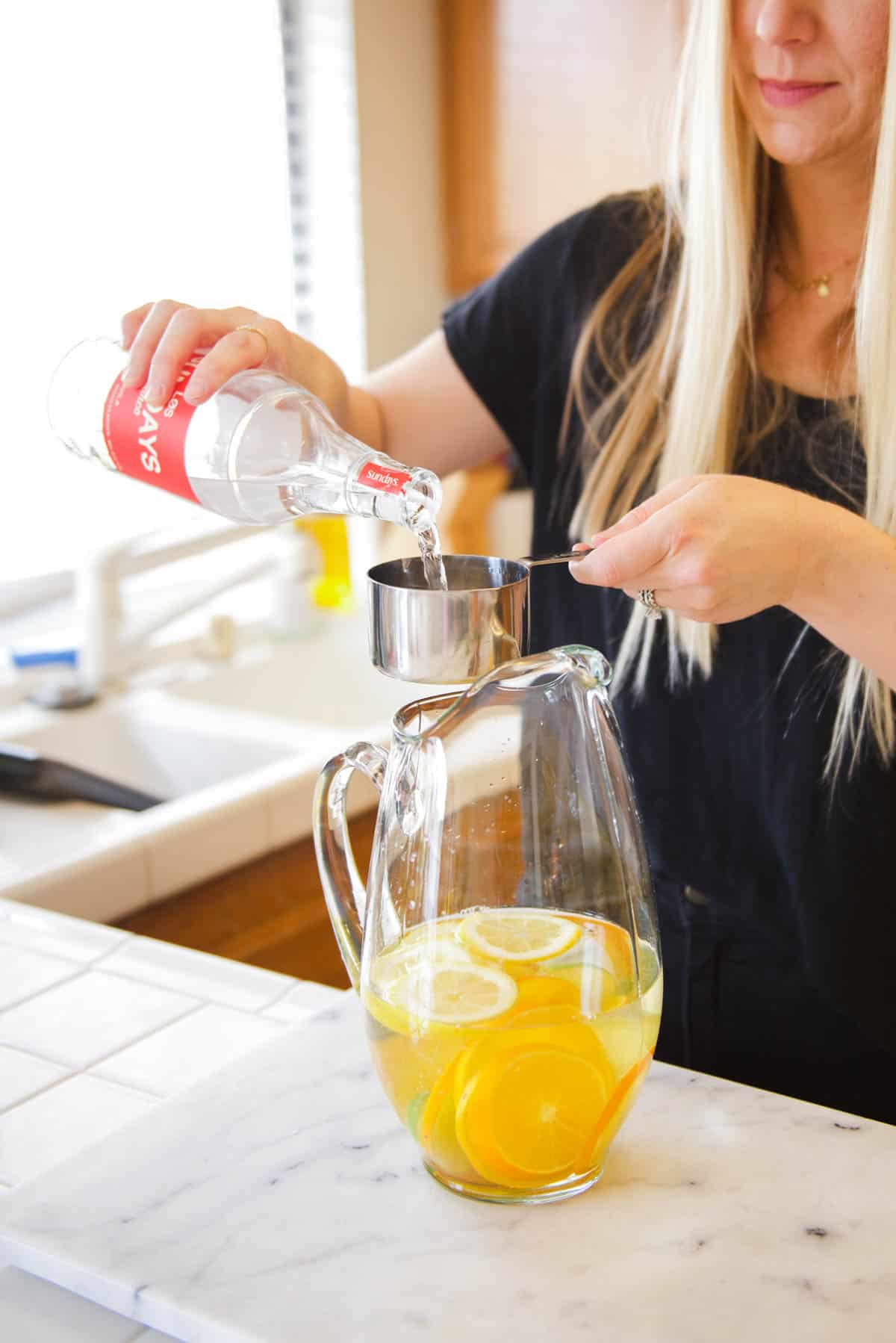 Woman measuring tequila to add to a glass pitcher for a wine cocktail. 