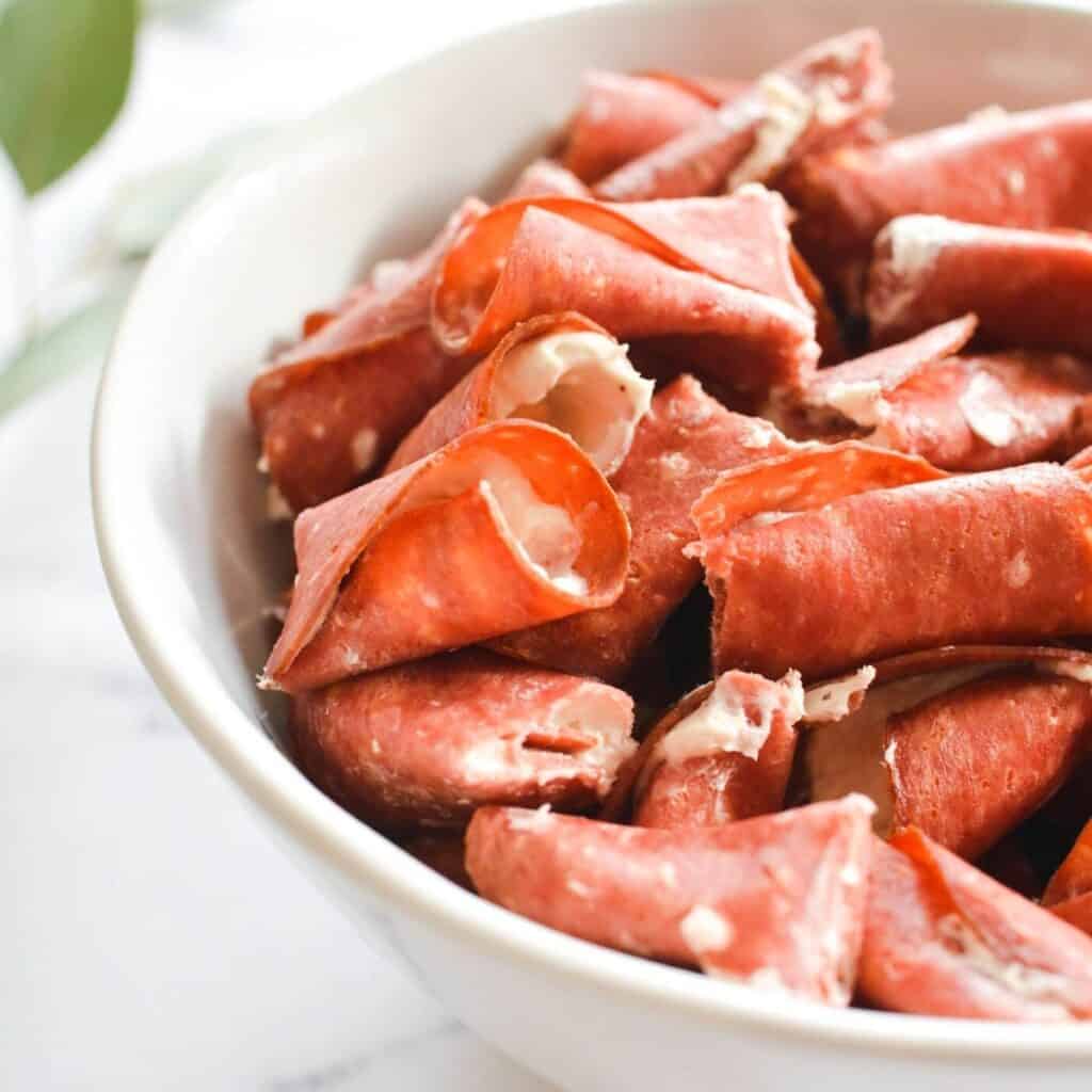 Close up of a white serving bowl with cut up Dried Beef Roll Ups.