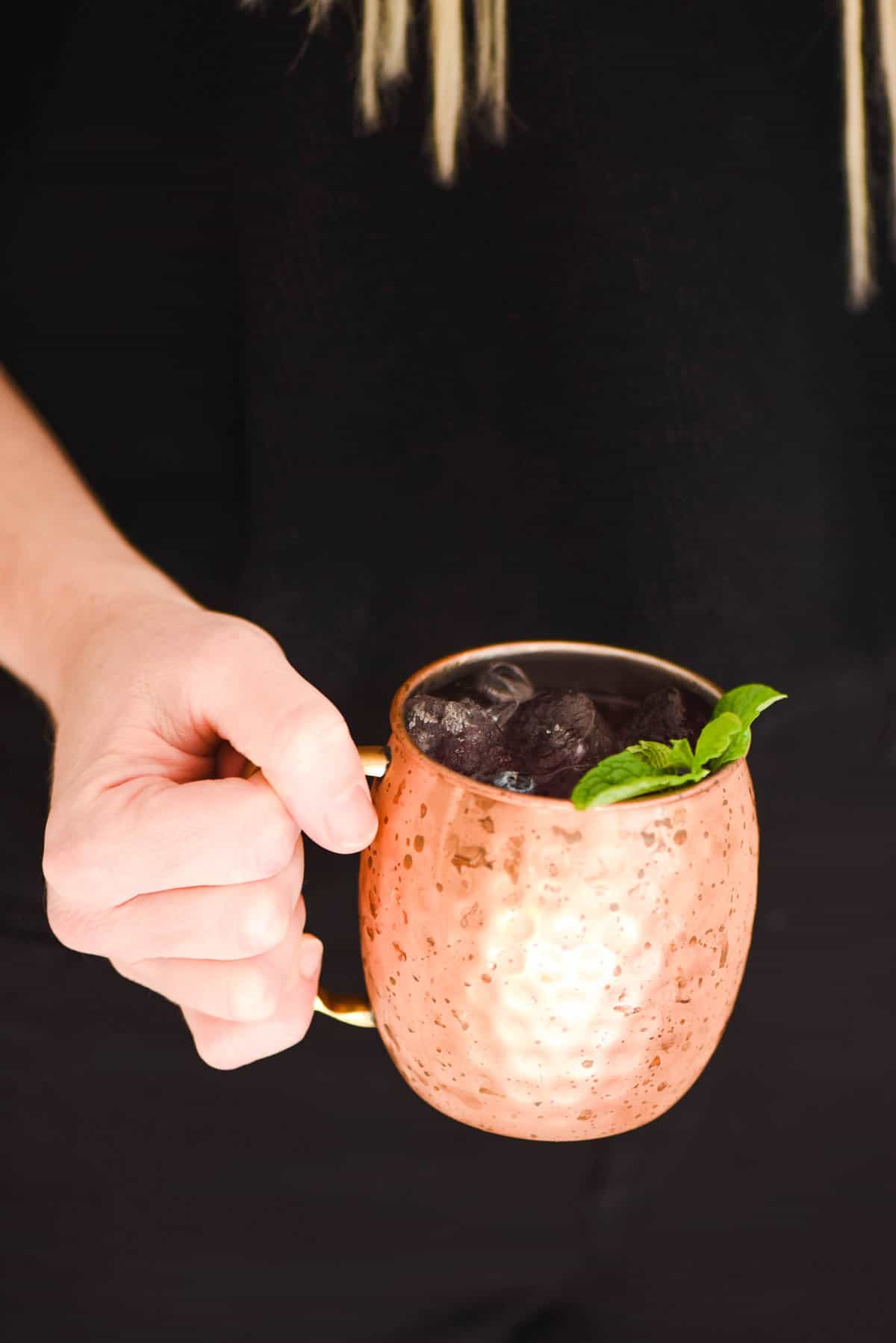Women holding a copper mug full of delicious Blueberry Mule Cocktail. 