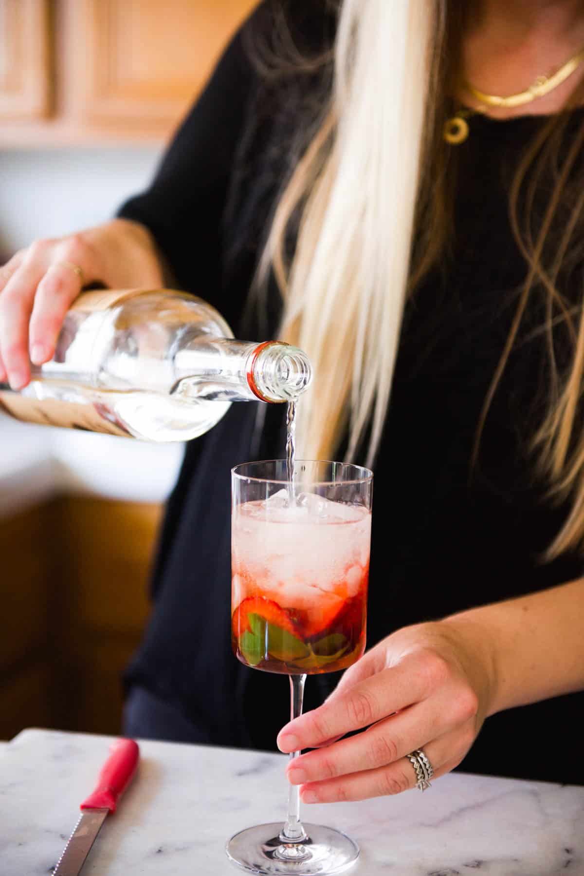 Woman adding vodka to a cocktail in a wine glass.