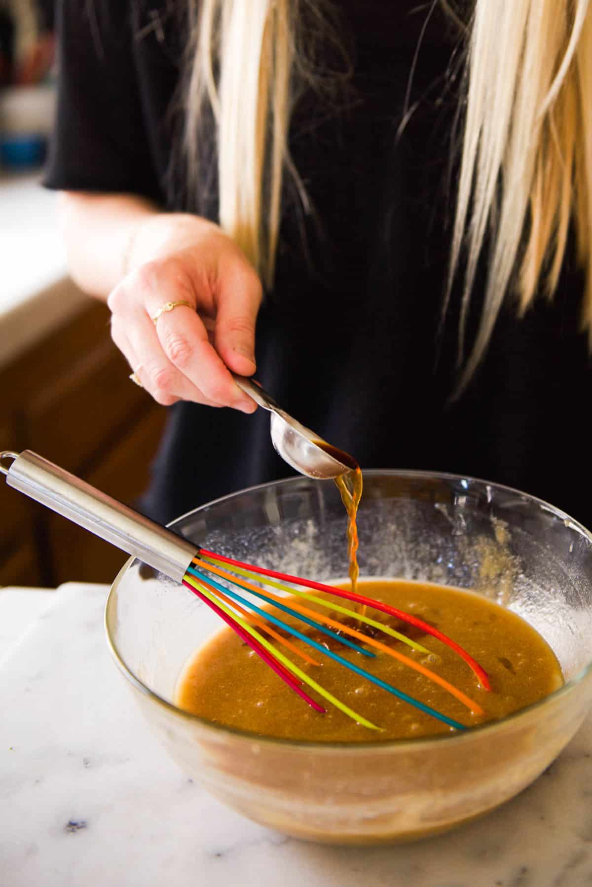 Woman adding vanilla to batter in a glass mixing bowl.
