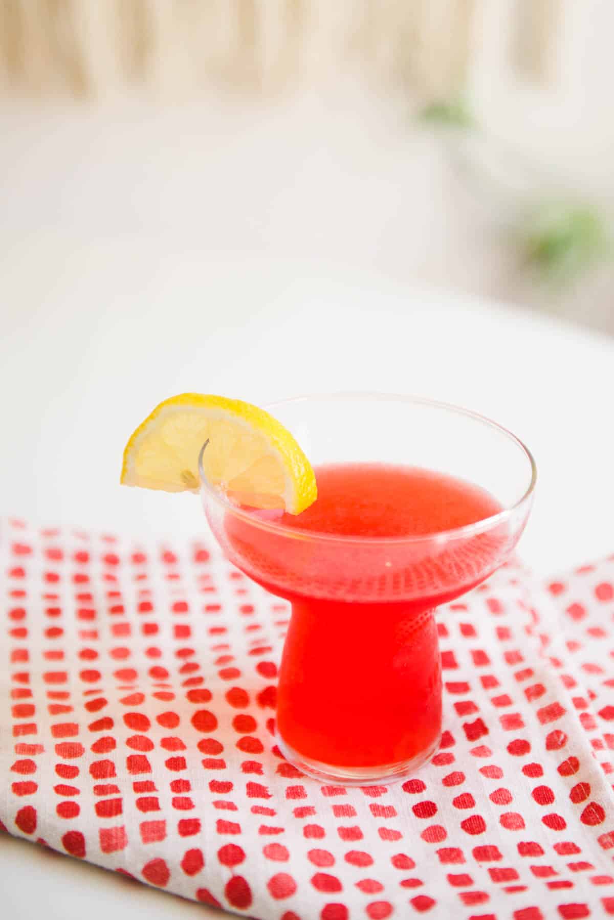 A glass on a cloth napkin on a table with a bright pink cocktail in it.