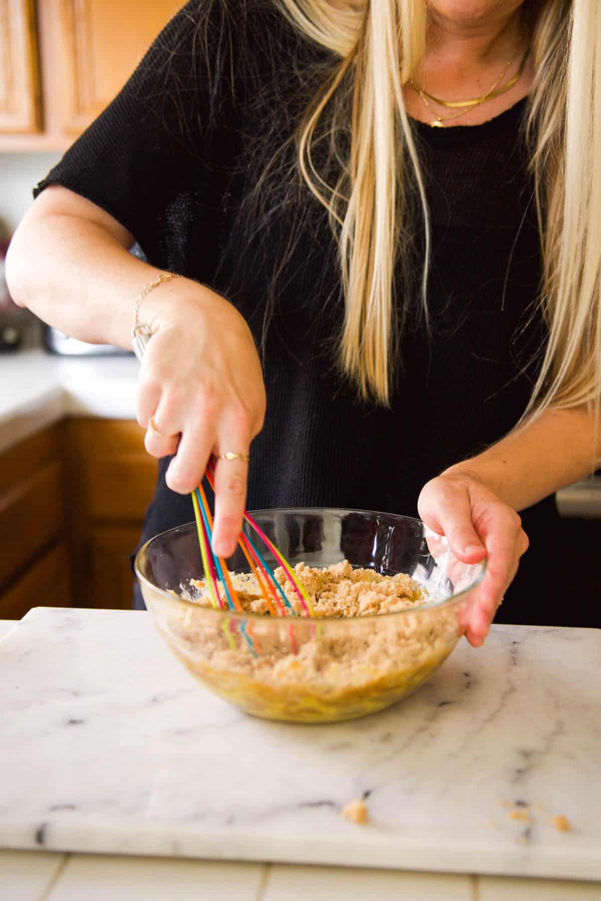 A woman mixing brown sugar into eggs with a whisk.