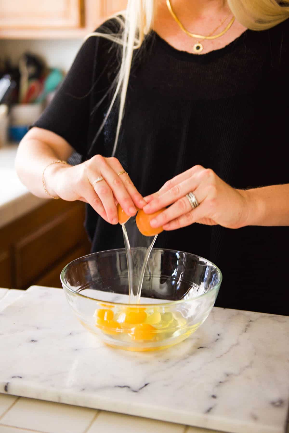 A woman cracking eggs into a large glass mixing bowl on the counter.