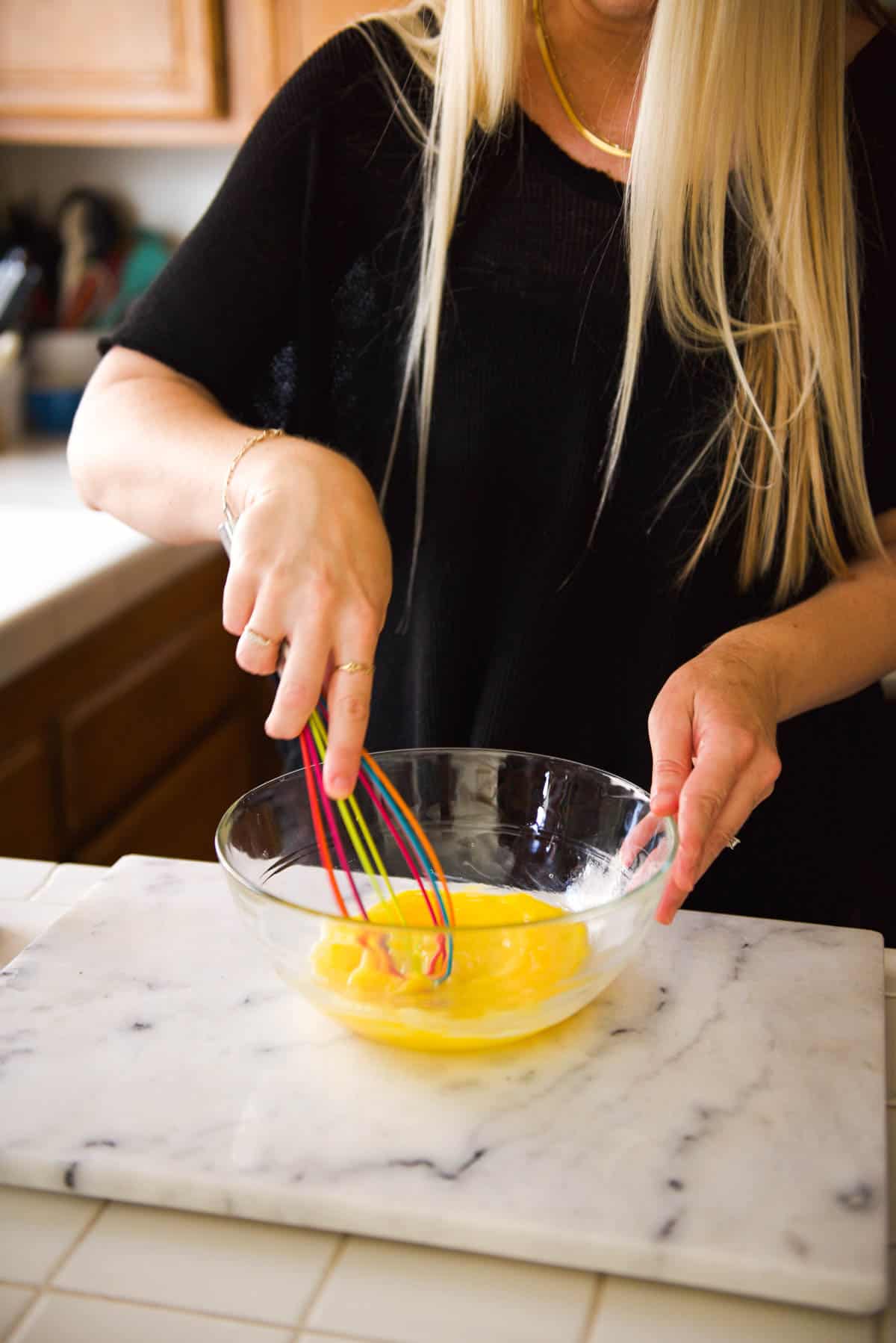 A woman whisking eggs in a large glass bowl on the counter.