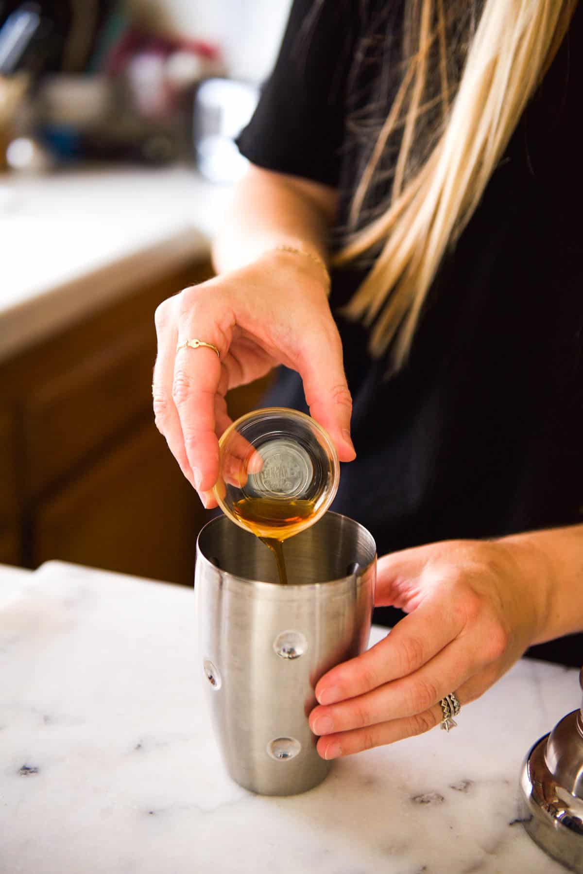 Adding maple syrup to a cocktail shaker.