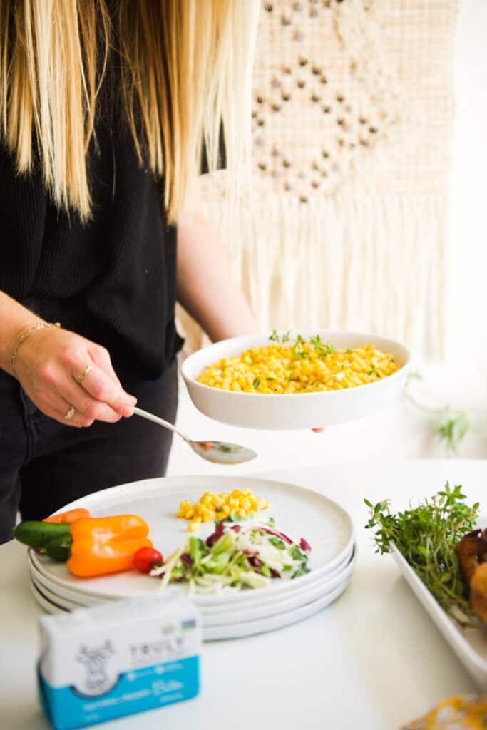 Woman putting a portion of corn on her plate with a spoon.