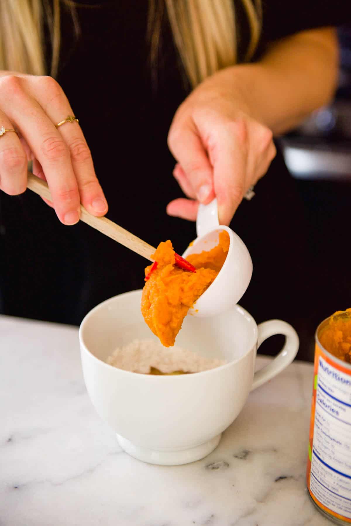 Adding pumpkin puree to a mug for a microwave cake for one.