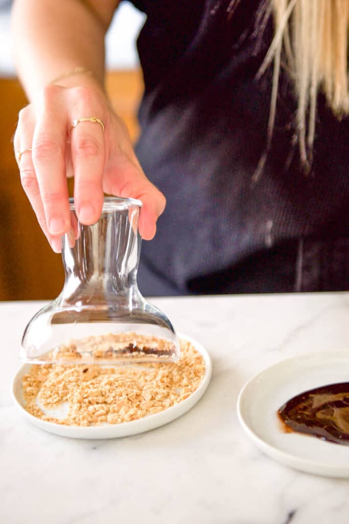 Dipping a chocolate rim of a cocktail glass into crushed graham crackers.