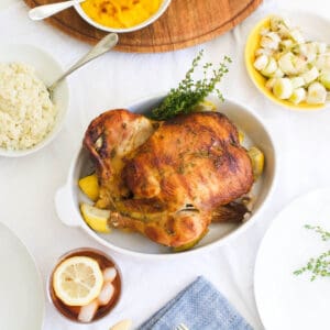 Close up of a rotisserie chicken in a baking dish on a dinner table.