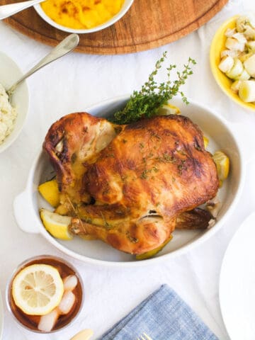 Close up of a rotisserie chicken in a baking dish on a dinner table.