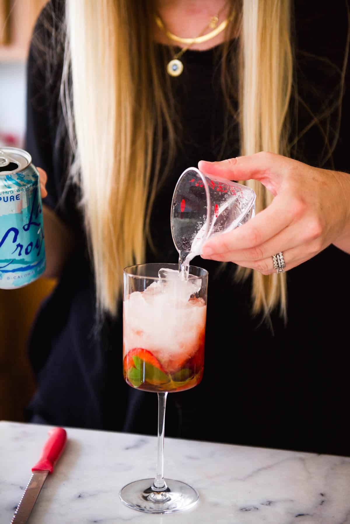 Pouring club soda from a measuring cup into a wine glass.