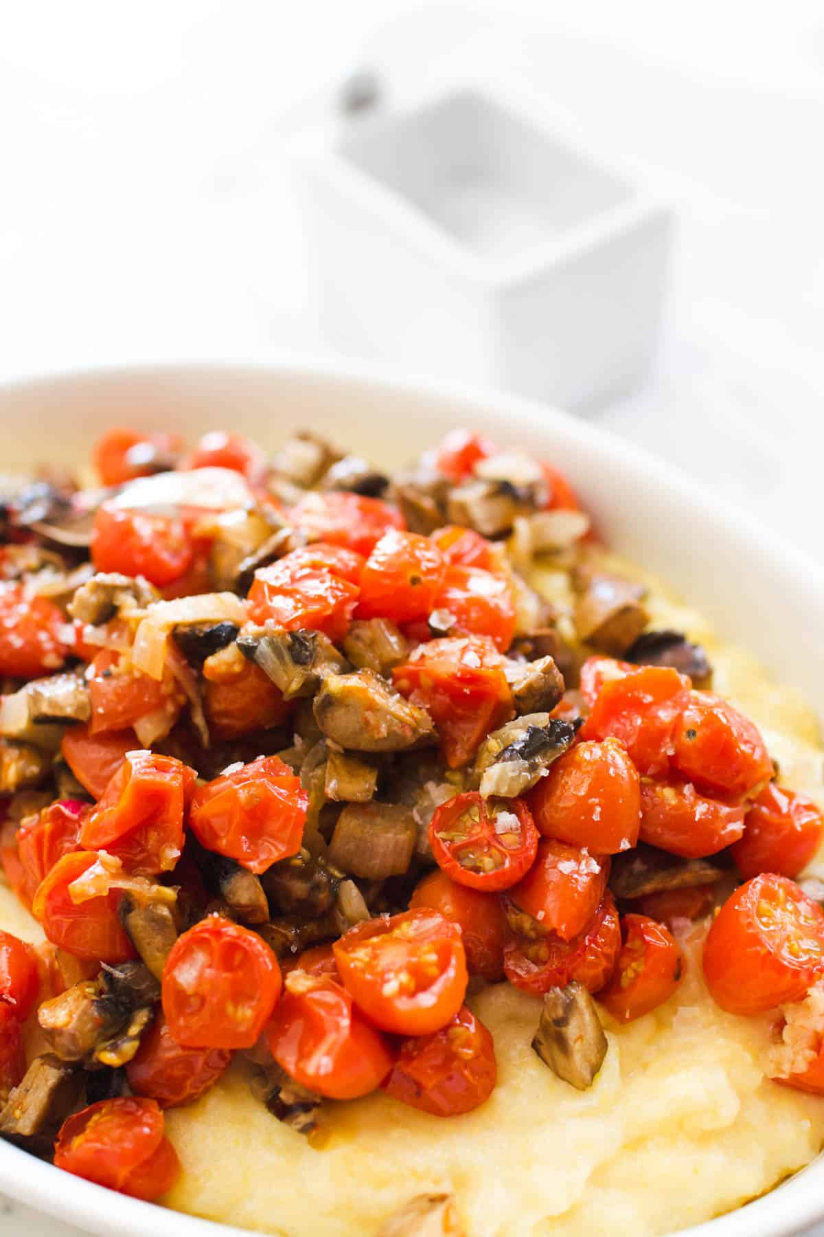 Close up of tomatoes and mushrooms on top of polenta sprinkled with sea salt.