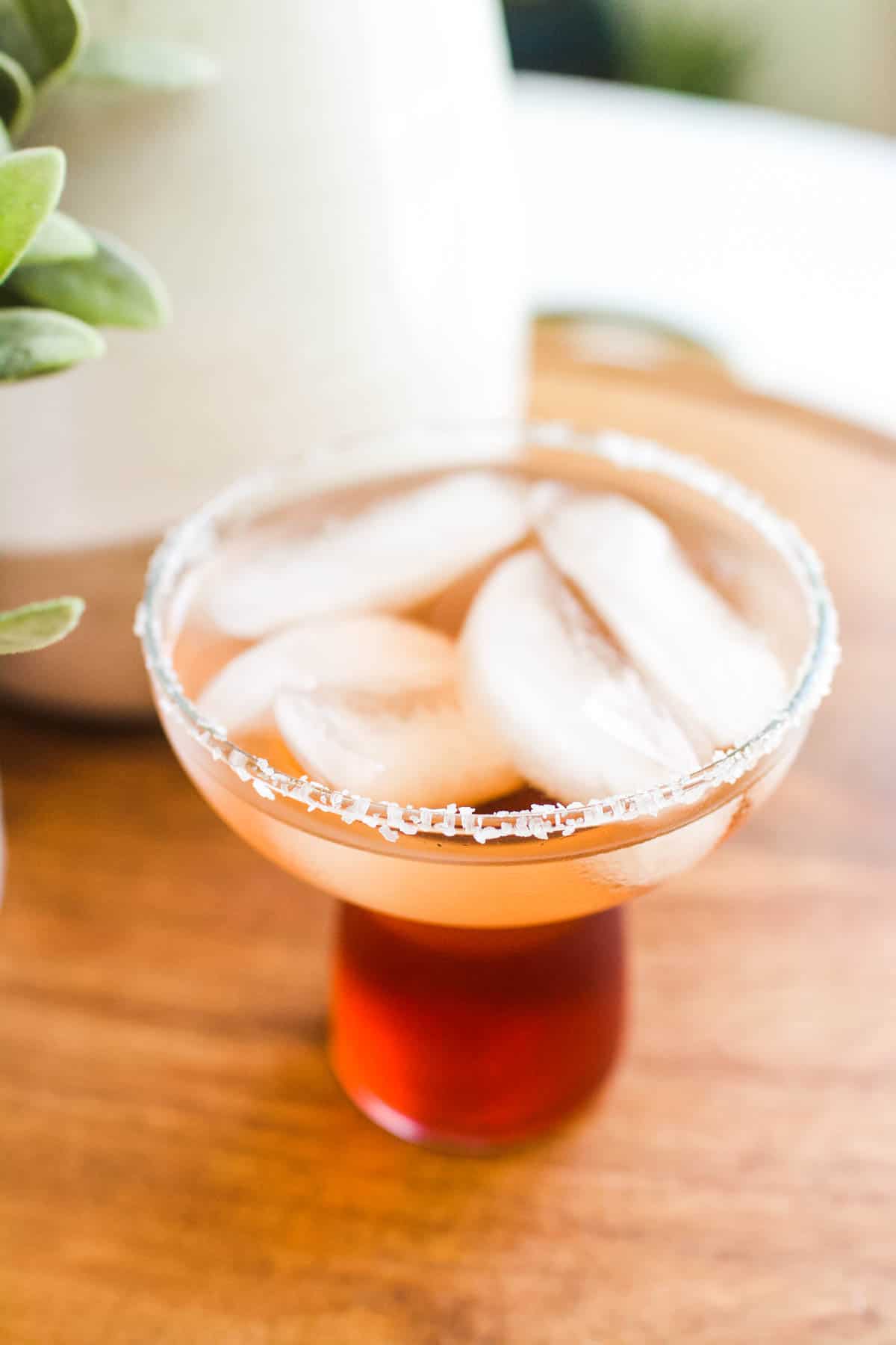 A salt rimmed cocktail glass on a table with a cocktail. 