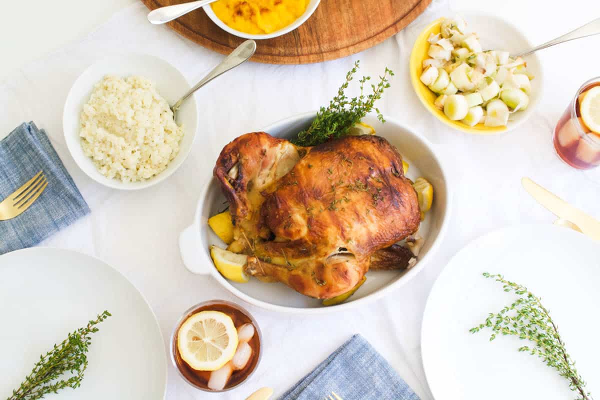 A roast store-bought chicken on a table with side dishes around it.