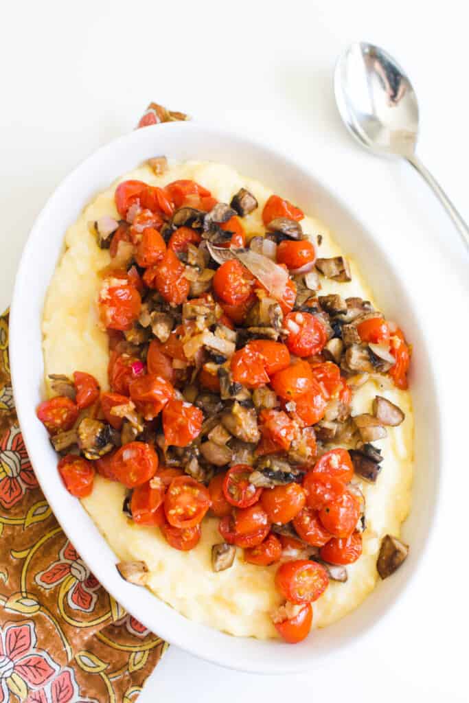 Overhead shot of a serving dish with roasted tomatoes and mushrooms on top of creamy polenta.