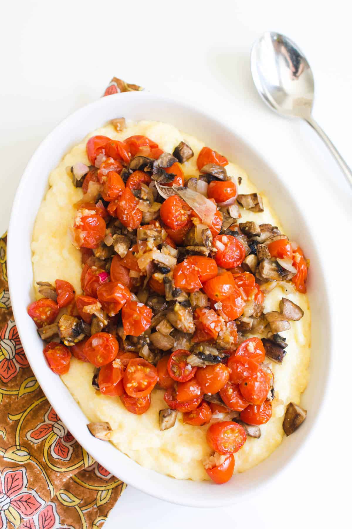 Overhead shot of a serving dish with roasted tomatoes and mushrooms on top of creamy polenta.