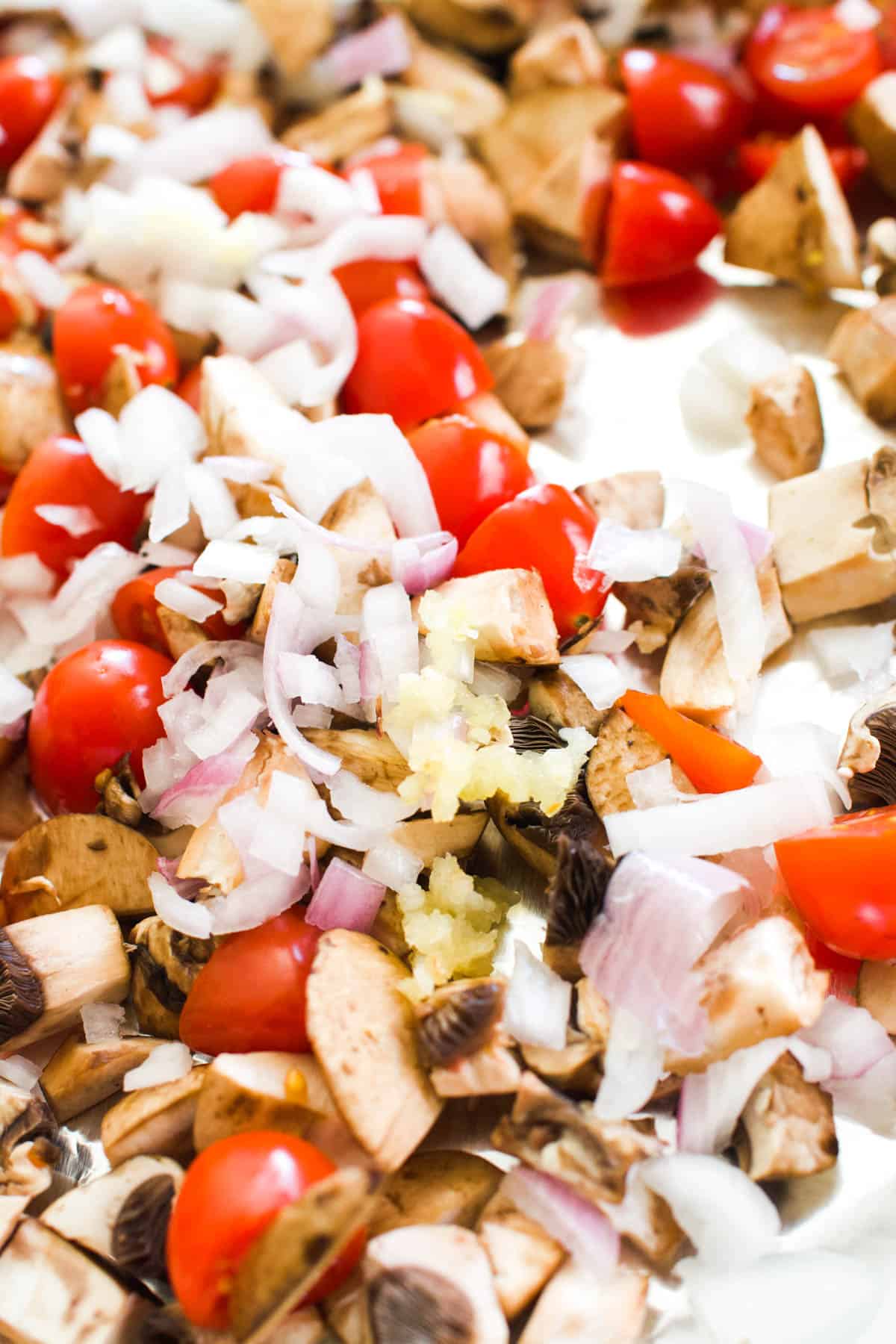 Close up of chopped mushrooms, tomatoes, chopped shallots and crushed garlic.